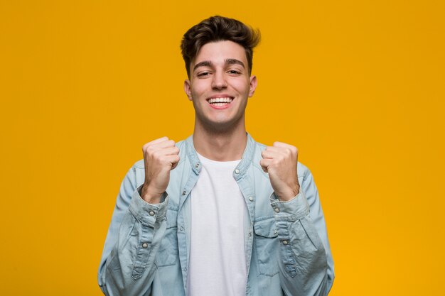 Foto joven estudiante guapo con una camisa de mezclilla animando despreocupado y emocionado. concepto de victoria