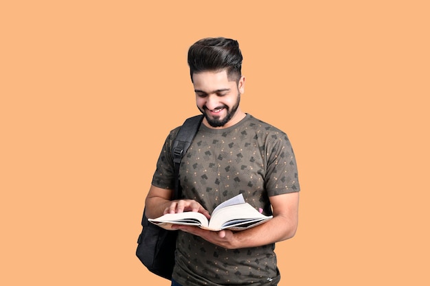 Joven estudiante guapo con camiseta sosteniendo un libro sonriendo modelo paquistaní indio