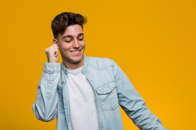 Joven estudiante guapo vistiendo una camisa vaquera bailando y divirtiéndose.