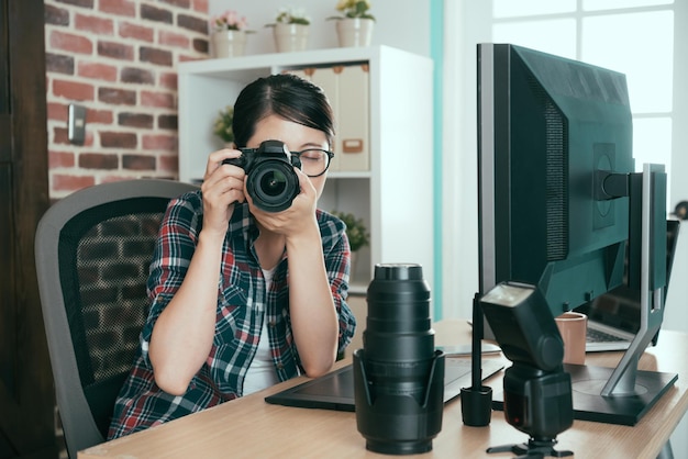 joven estudiante hermosa que practica la práctica de la cámara profesional tomando fotos de negocios sentada en el escritorio de la oficina de trabajo de la compañía de fotógrafos.