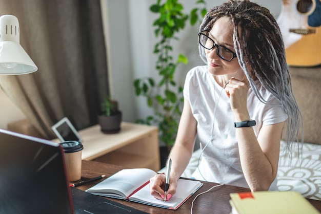 Una joven estudiante hermosa con rastas está estudiando en una lección en línea en casa en una computadora portátil