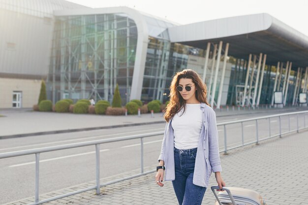 Una joven estudiante hermosa sale del aeropuerto en una nueva ciudad y espera un taxi