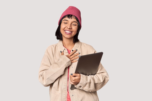 Joven estudiante hispano con una computadora portátil en el estudio cubriendo las orejas con las manos