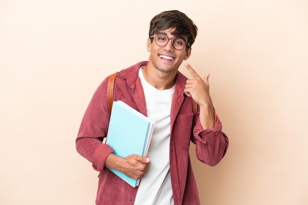 Joven estudiante hombre caucásico aislado sobre fondo ocre dando un pulgar hacia arriba gesto