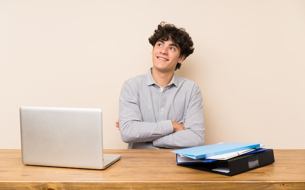 Joven estudiante hombre con una computadora portátil mirando hacia arriba mientras sonríe