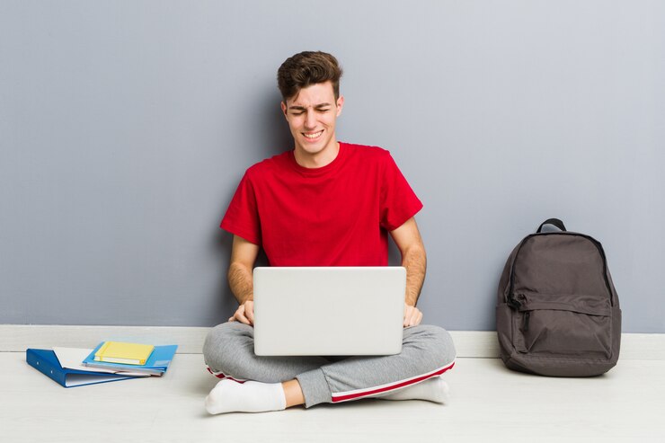 Foto joven estudiante hombre sentado en el piso de su casa sosteniendo una computadora portátil