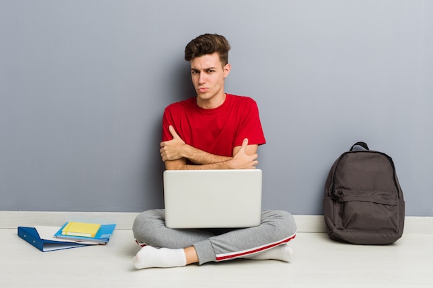 Joven estudiante hombre sentado en el piso de su casa sosteniendo una computadora portátil