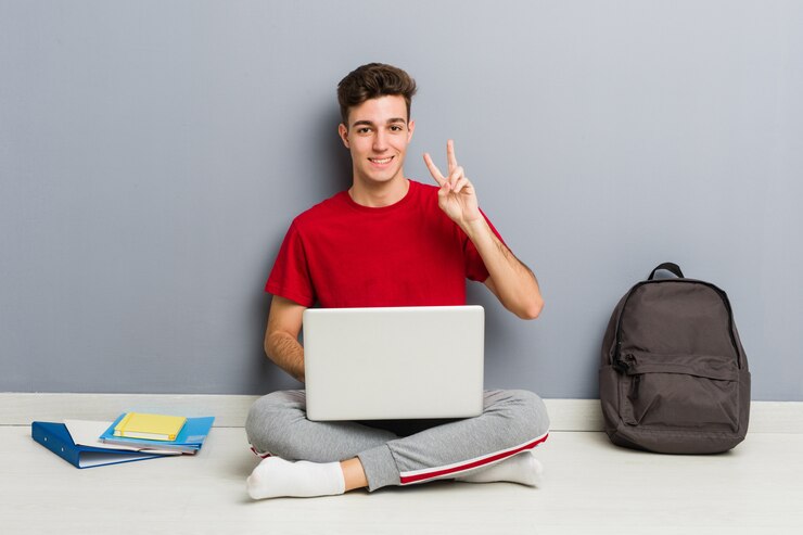 Foto joven estudiante hombre sentado en el piso de su casa sosteniendo una computadora portátil