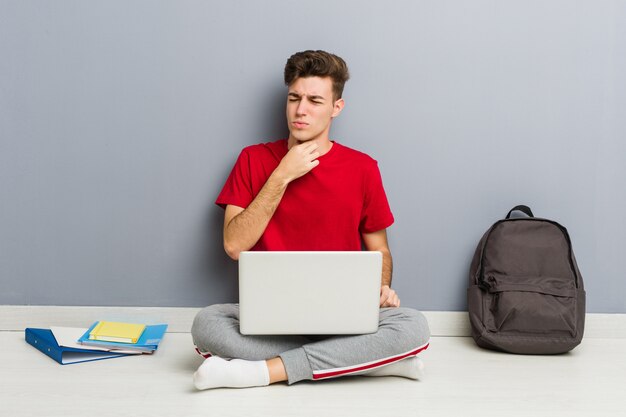 Joven estudiante hombre sentado en el piso de su casa sosteniendo una computadora portátil