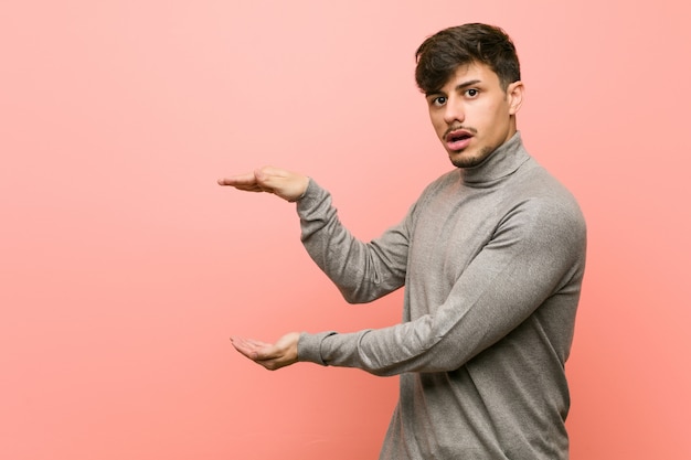 Joven estudiante inteligente hombre sorprendido y sorprendido sosteniendo un espacio de copia entre las manos.