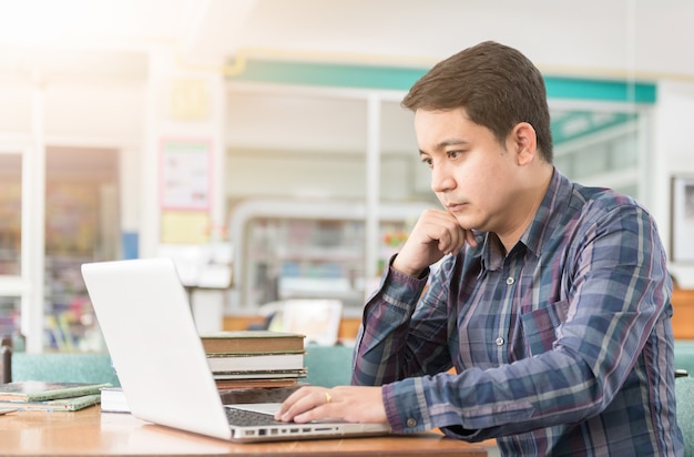 Foto joven estudiante jugar computadora y preparar examen y aprender lecciones en la biblioteca de la escuela, haciendo resea