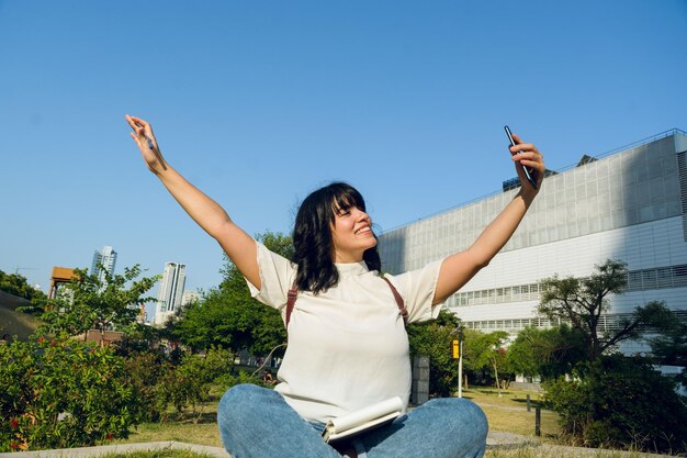 Joven estudiante latina mirando su teléfono muy feliz por sus éxitos