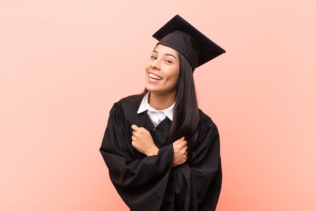 Joven estudiante latina sonriendo alegremente y celebrando, con los puños cerrados y los brazos cruzados, sintiéndose feliz y positiva