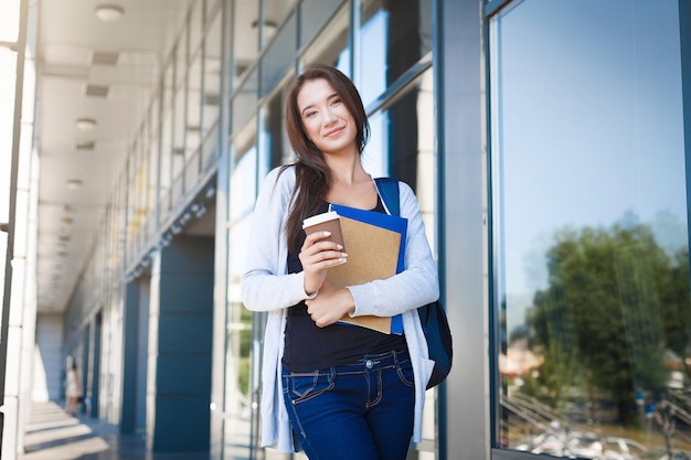 Joven estudiante, con libros y mochila. Quedarse afuera antes de la lección y tomar café. Pensando en el próximo día. Concepto de estilo de vida y educación.