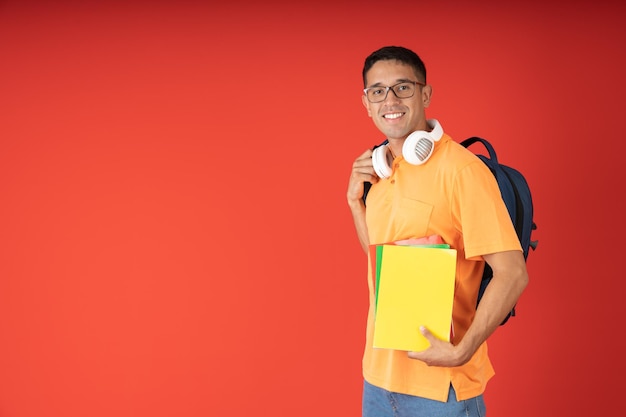 Joven estudiante masculino con gafas cargando su mochila y sus cuadernos