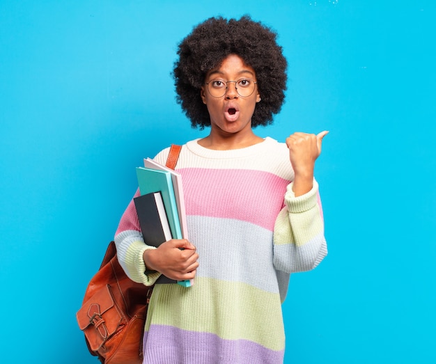 Joven estudiante mujer afro mirando asombrada con incredulidad, señalando un objeto en el costado y diciendo wow, increíble