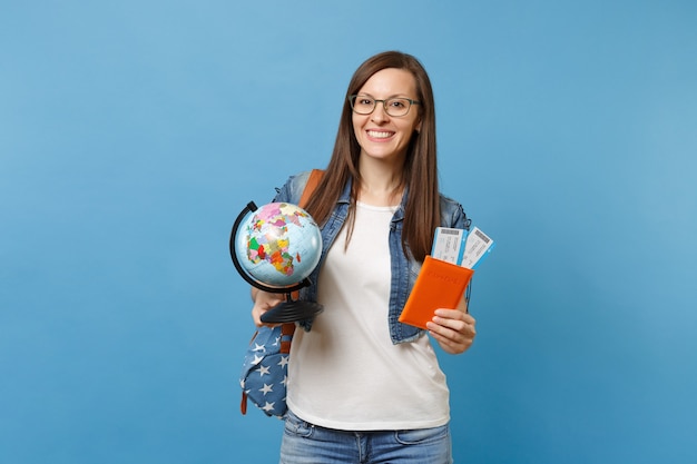 Joven estudiante mujer alegre en vasos con mochila con guante mundial, pasaporte, boletos de tarjeta de embarque aislados sobre fondo azul. Educación en colegio universitario en el extranjero. Concepto de vuelo de viajes aéreos.