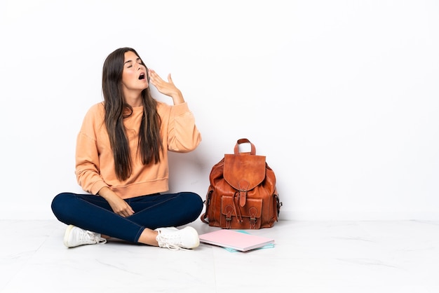 Joven estudiante mujer brasileña sentada en el suelo bostezando y cubriendo la boca abierta con la mano