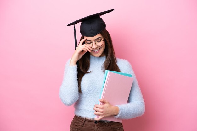 Joven estudiante mujer brasileña vistiendo sombrero graduado aislado sobre fondo rosa riendo