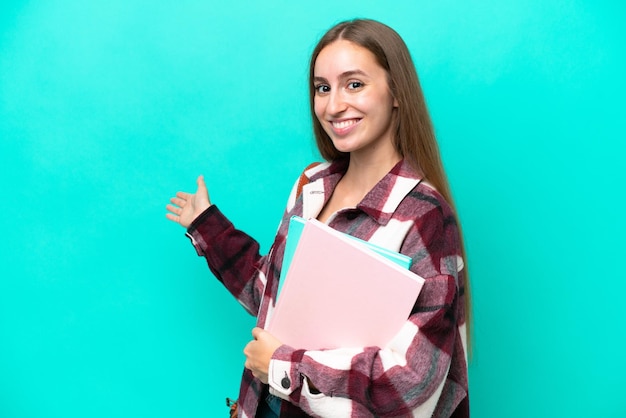 Joven estudiante mujer caucásica aislada de fondo azul extendiendo las manos a un lado para invitar a venir