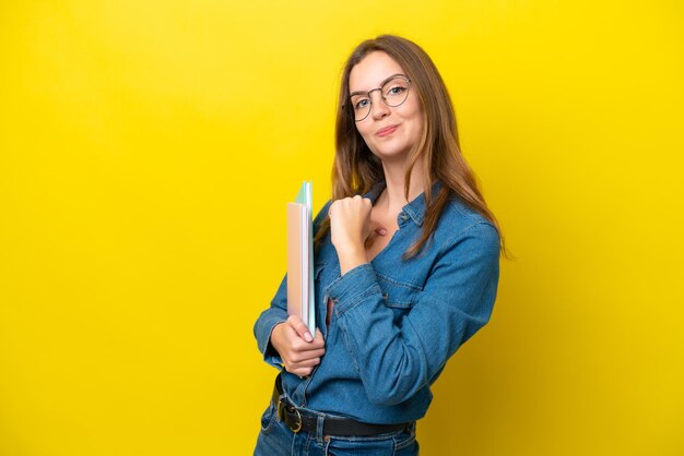 Foto joven estudiante mujer caucásica aislada sobre fondo amarillo orgullosa y satisfecha