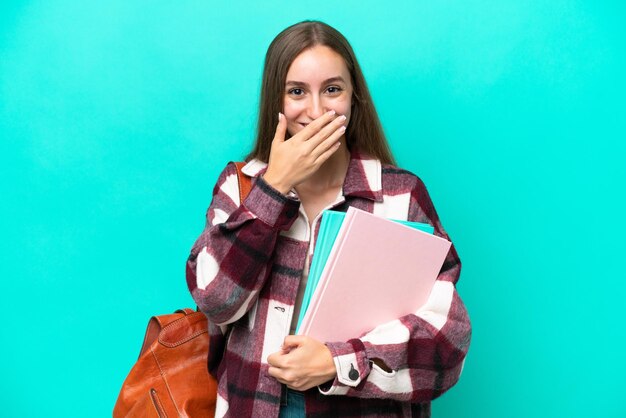 Joven estudiante mujer caucásica aislada sobre fondo azul feliz y sonriente cubriendo la boca con la mano