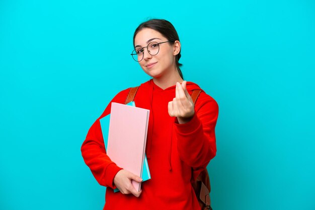 Joven estudiante mujer caucásica aislada sobre fondo azul haciendo gesto de dinero