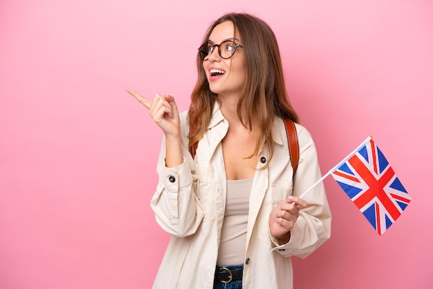 Joven estudiante mujer caucásica sosteniendo una bandera del Reino Unido aislada en un fondo rosado con la intención de darse cuenta de la solución mientras levanta un dedo