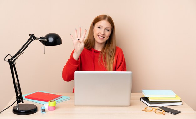 Joven estudiante mujer en un lugar de trabajo con una computadora portátil feliz y contando cuatro con los dedos