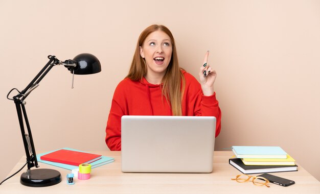 Joven estudiante mujer en un lugar de trabajo con una computadora portátil con la intención de darse cuenta de la solución mientras levanta un dedo