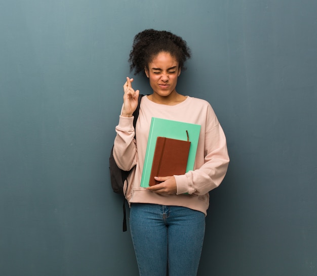 Joven estudiante mujer negra cruzando los dedos para tener suerte. Ella está sosteniendo libros.