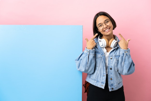 Foto joven estudiante mujer de raza mixta con una gran pancarta sobre antecedentes aislados dando un gesto de pulgar hacia arriba