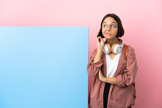 Joven estudiante mujer de raza mixta con una gran pancarta sobre antecedentes aislados manteniendo una conversación con el teléfono móvil