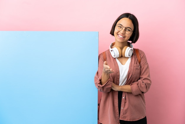 Joven estudiante mujer de raza mixta con una gran pancarta sobre pared aislada estrecharme la mano para cerrar un buen trato