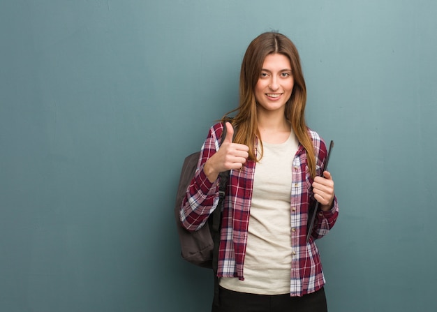 Joven estudiante mujer rusa sonriendo y levantando el pulgar hacia arriba