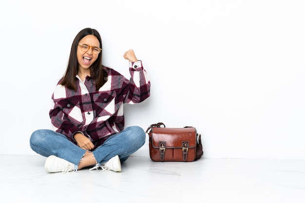 Joven estudiante mujer sentada en el piso celebrando una victoria