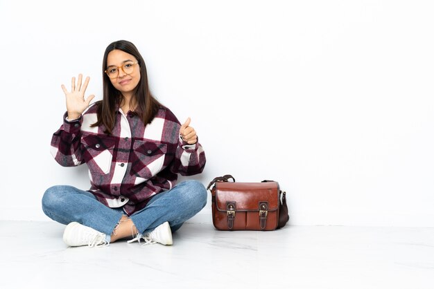 Joven estudiante mujer sentada en el suelo contando seis con los dedos