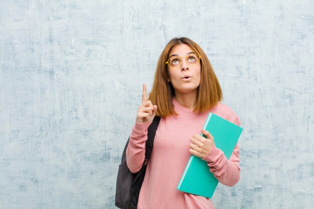 Joven estudiante mujer sorprendida, sorprendida y con la boca abierta, apuntando hacia arriba con ambas manos para copiar espacio