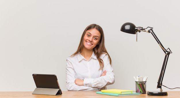 Joven estudiante mujer trabajando en su escritorio cruzando los brazos, sonriente y relajado