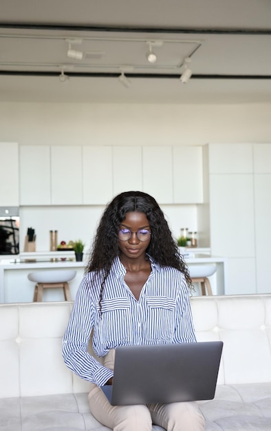 Joven estudiante negra inteligente de carreras mixtas sentada escribiendo usando una computadora portátil