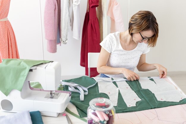 Joven estudiante de niña bonita estudia en un diseñador de ropa en la universidad y hace su primera tesis sentada en un escritorio con una máquina de coser. Concepto de diseño de ropa.