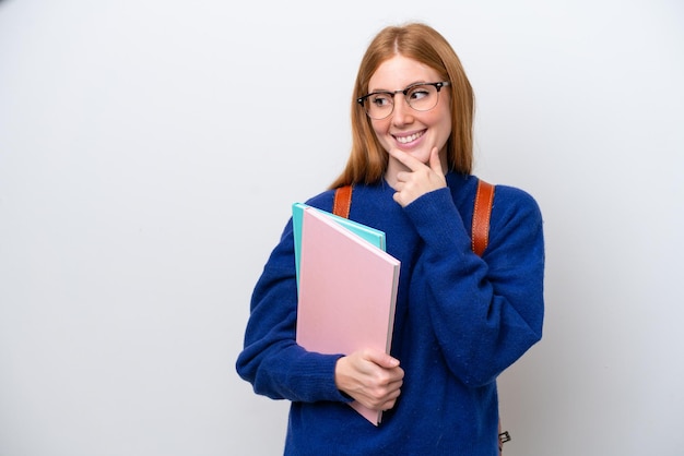 Foto joven estudiante pelirroja mujer aislada sobre fondo blanco mirando hacia el lado y sonriendo