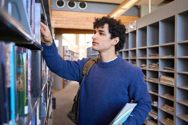 Joven estudiante de posgrado seleccionando un libro de una estantería en el campus de la biblioteca