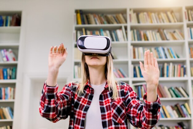 Joven estudiante rubia caucásica trabajando con simulador de realidad virtual en la biblioteca.