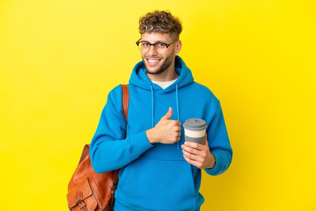 Joven estudiante rubio aislado de fondo amarillo dando un gesto de pulgar hacia arriba