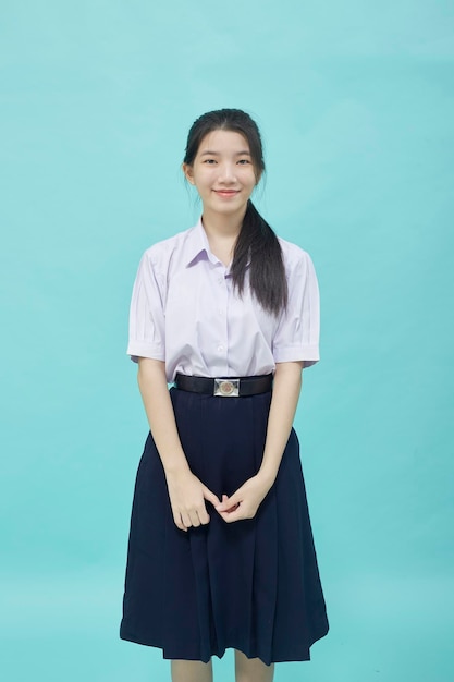 Joven estudiante de secundaria asiática chica en uniforme de estudiante sobre fondo azul claro studio aislado