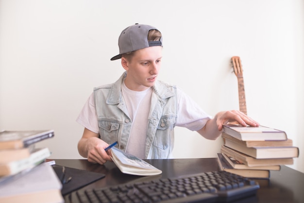 Joven estudiante se sienta a la mesa con libros y estudios. El adolescente está haciendo la tarea