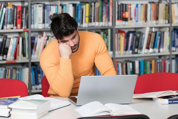 Joven estudiante se siente aburrido mientras intenta estudiar los exámenes de ingreso a la universidad o la universidad