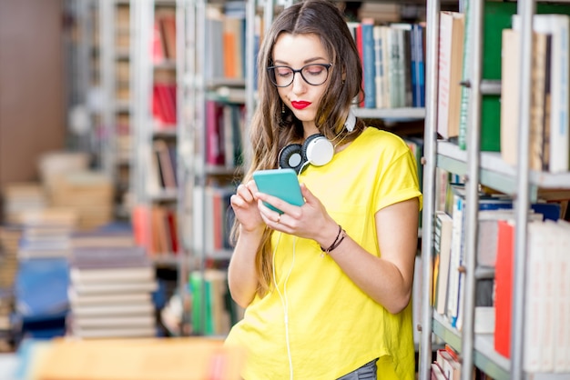 Joven estudiante con teléfono inteligente en la biblioteca