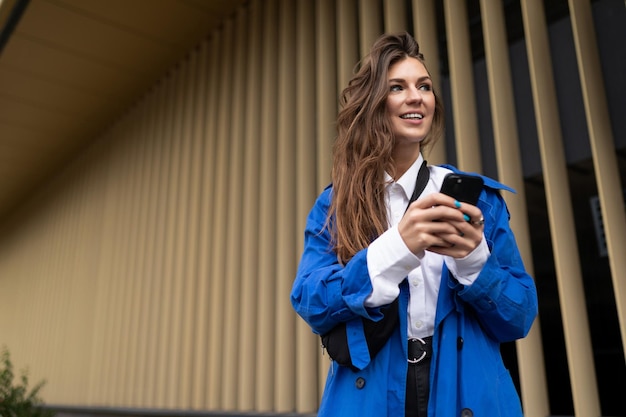 Joven estudiante con un teléfono móvil mirando a lo lejos con una sonrisa contra el